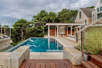 Pool with stone coping and a wood deck beside a pool house