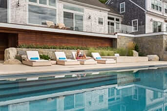 Poolside lounge chairs beside a shingled coastal home